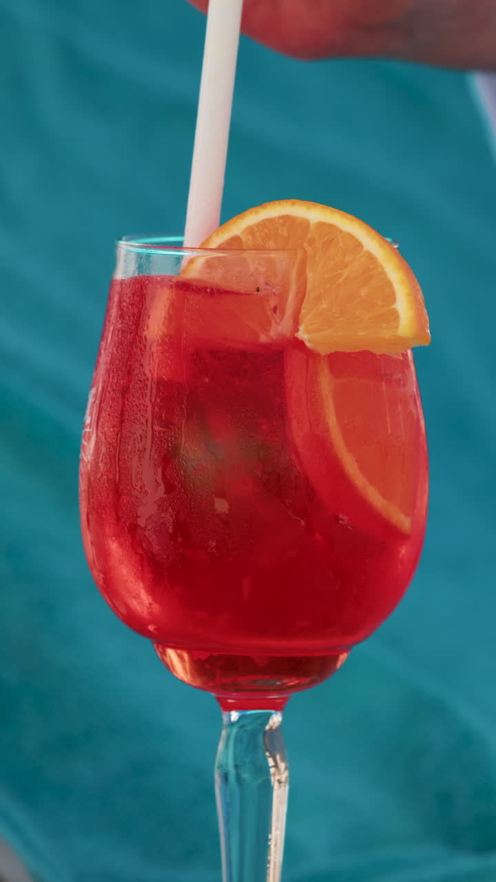 Close up of a refreshing red orange cocktail with orange slice and ice cubes, captured outdoors on a sunny day in Cannes. Vertical
