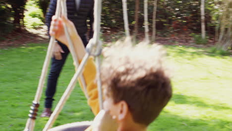 father and son having fun on tyre swing in garden at home