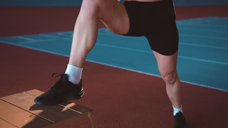 focused blonde sportswoman warming up and stretching legs in an indoor sport facility