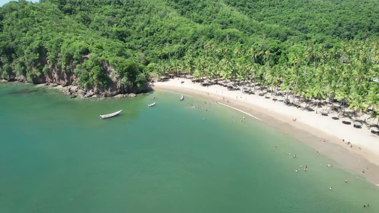 Drone shot of a beautiful remote tropical bay with palm trees, sandy beach, and a few people enjoying the water