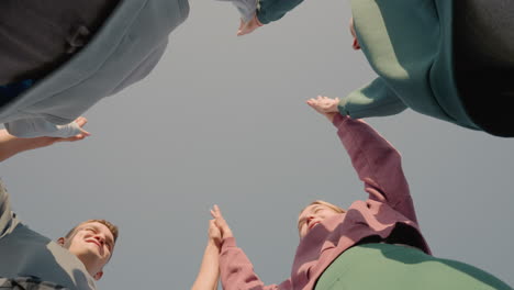 upward view of team members clapping hands together in a moment of joy and unity under clear sky, symbolizing teamwork, support, and positive energy as they celebrate collaboration