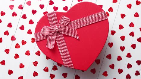 Boxed-gift-placed-on-heart-shaped-red-sequins-on-white-wooden-table