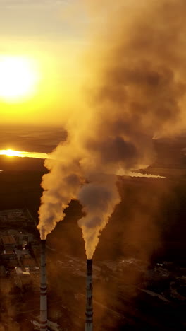 aerial view on the industrial factory. power plant near the river on the natural landscape at sunset. large pipes with smoke in the evening. vertical video