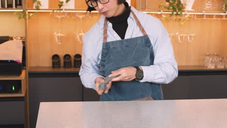 waiter cleaning bar counter with a cloth and then smiling at camera with his colleague