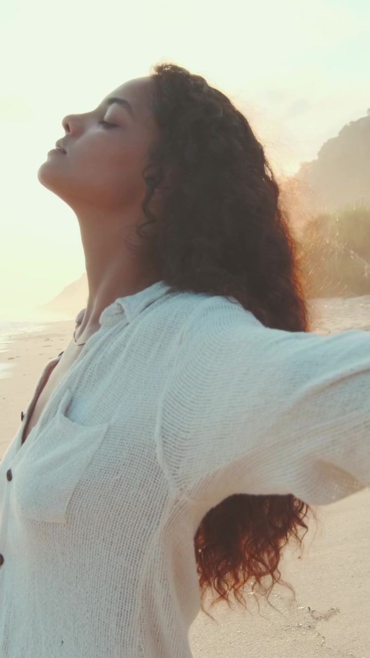 Mujer de pie en la playa con los brazos abiertos durante el atardecer cerca de las olas del océano