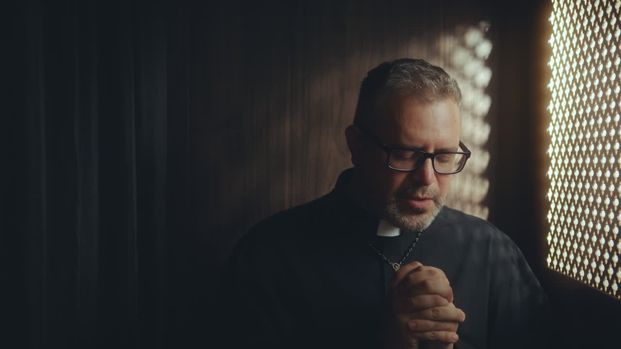 Clergyman Praying in Dimly Lit Confessional Booth