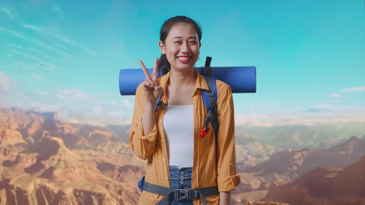 Asian Female Hiker With Mountaineering Backpack Smiling And Showing Peace Gesture While Traveling At The Top Of Mountain