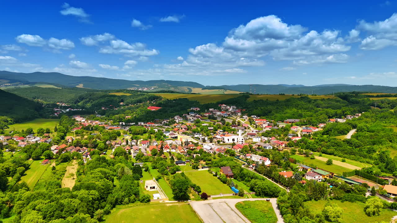 Daytime European village view. A vibrant village nestled among green hills showcases charming homes and lush countryside under a bright blue sky