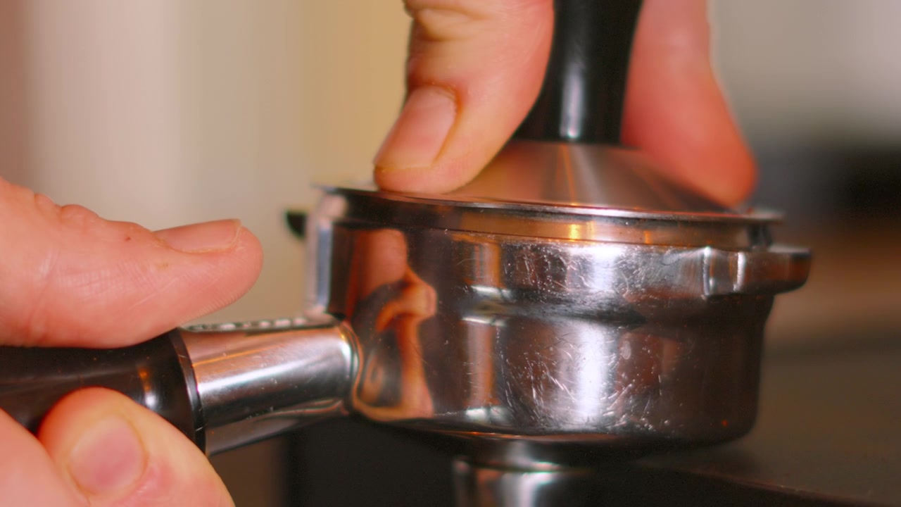 Kaffeepulver wird im Siebträger mit einem Tamper verdichtet, bereit zur Verwendung in der Espressomaschine. Clip eines unabhängigen lokalen Unternehmens.