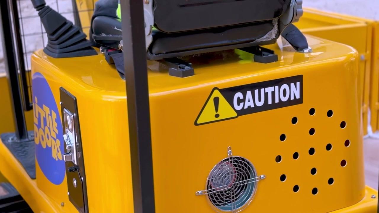 A close up shot of a yellow coin operated toy excavator. The stationary indoor children's ride features a black seat, a caution sticker, and a metal coin slot mechanism.