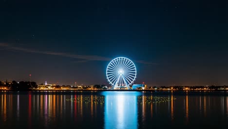 a stunning nighttime view of a colorful ferris wheel reflecting on water, illuminating the skyline with vibrant lights in a calm atmosphere under a starry sky