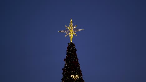 bright yellow star on the top of christmas tree with baubles sparkling on night sky background