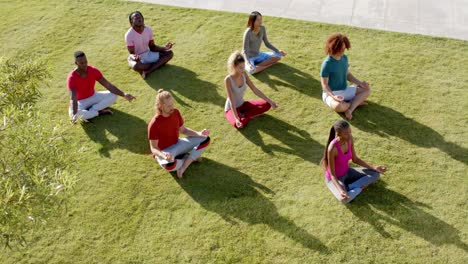 high angle view of diverse friends practicing yoga meditation sitting in sunny garden, slow motion