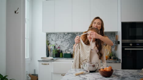 cheerful mother putting apron daughter in home kitchen. friendly family cooking