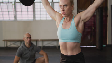 mujer caucásica en forma trabajando con barra con entrenador masculino en el gimnasio