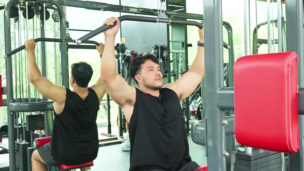 Two men perform strength training on gym machines in a well-lit fitness center, focusing on upper body exercises