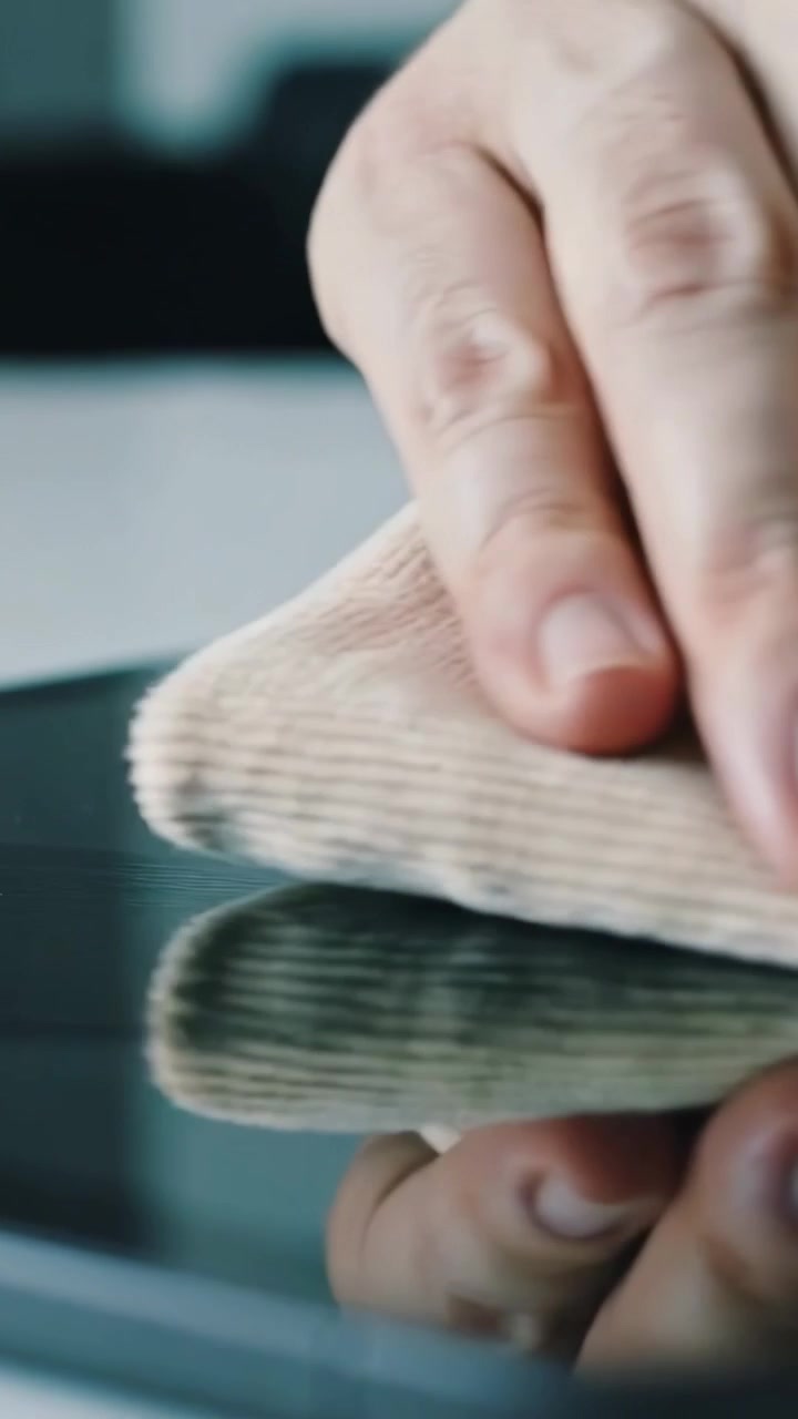 Vertical video: Grasping folded cloth, adult hands cleaning phone screen on desk, removing smudges