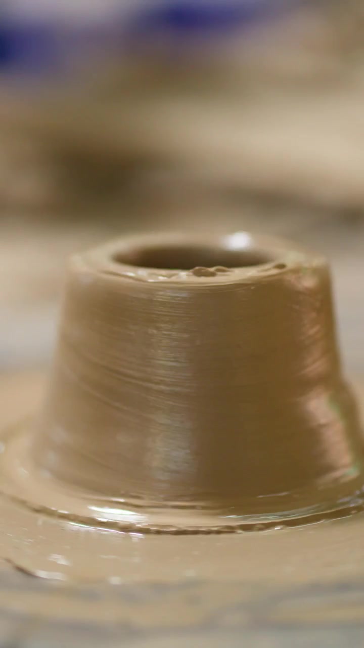 Close-up of a potter molding wet clay into a vessel on a spinning wheel.