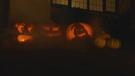 3 carved lit pumpkins outside the front of a house halloween with smoke slow motion