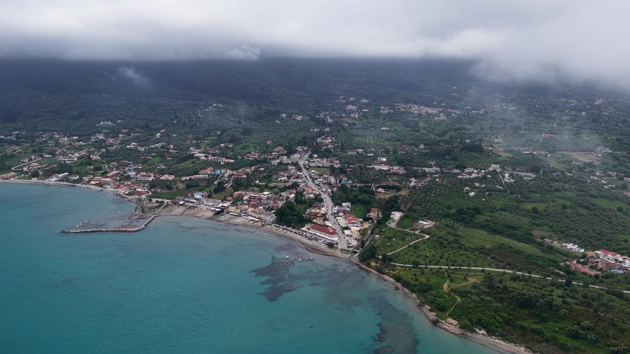 Volo cinematografico con drone sul villaggio costiero di Roda, nella Corfù settentrionale, con un piccolo porto peschereccio, il Mar Ionio e le montagne.