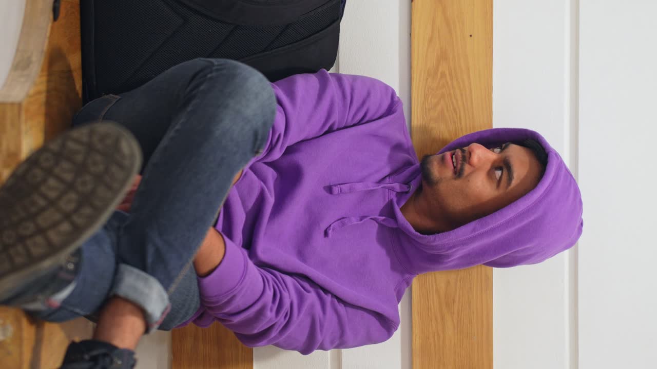 Vertical shot of man wearing purple hoodie talks to someone sitting on bench