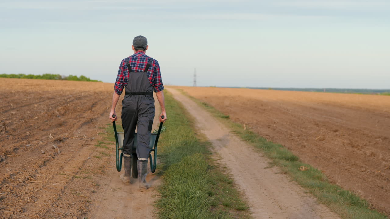 granjero empujando una carretilla en un camino de tierra a través de un campo