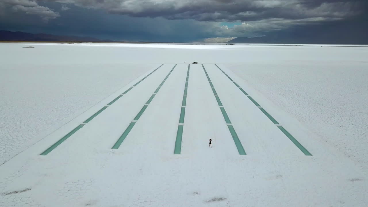 Aerial View of Female Silhouette on Massive Salt Flat Under Stormy Sky, Argentina, Salinas Grandes