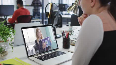 Caucasian-woman-having-a-video-call-with-female-office-colleague-on-laptop-at-office