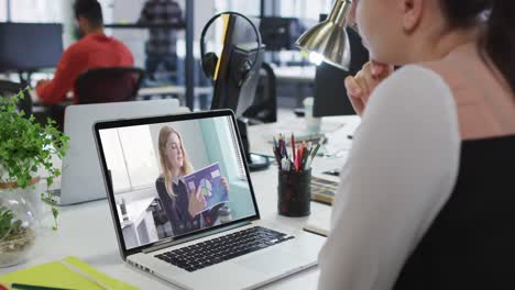 Mujer-Caucásica-Teniendo-Una-Videollamada-Con-Una-Colega-De-Oficina-En-Una-Computadora-Portátil-En-La-Oficina