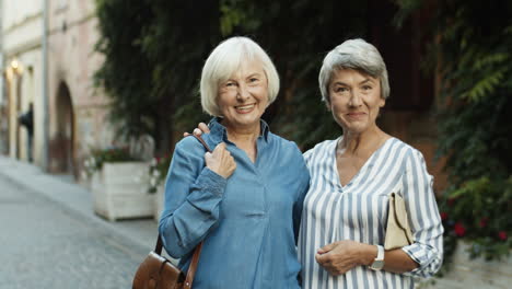 Retrato-De-Dos-Hermosas-Mejores-Amigas-Paradas-En-La-Calle-De-La-Ciudad,-Abrazándose-Y-Sonriendo-A-La-Cámara