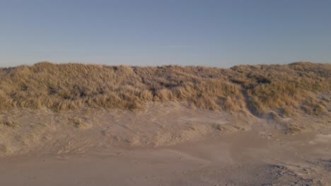 sandy beach and dunes on ocean coastline, aerial side fly cinematic shot