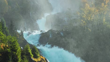 water rushes over jagged rocks, creating a cloud of mist as it crashes into the river below