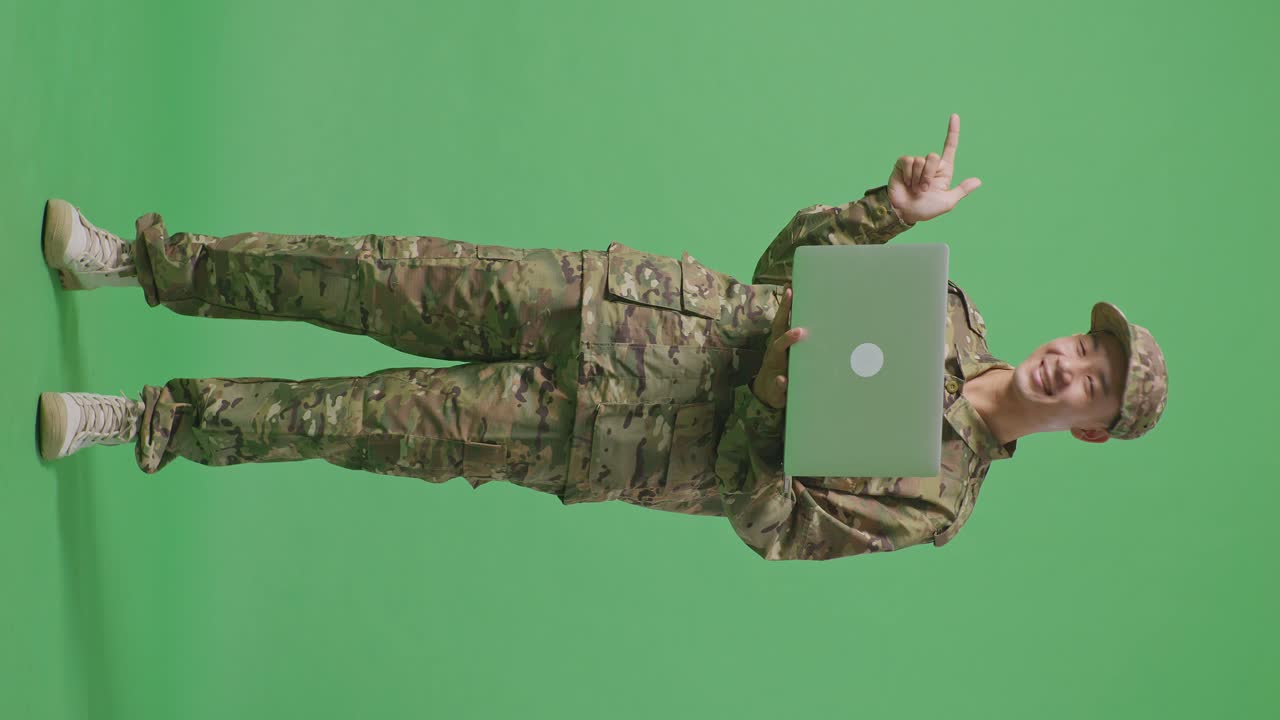 Full Body Of Asian Man Soldier Using A Laptop And Pointing To Side While Standing In The Green Screen Background Studio