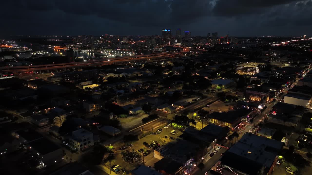 Aerial flight over city suburb of tampa at night. Lighting lantern and streetlamps along streets. Downtown skyline in distance. Florida, United States at midnight. Backwards drone shot.