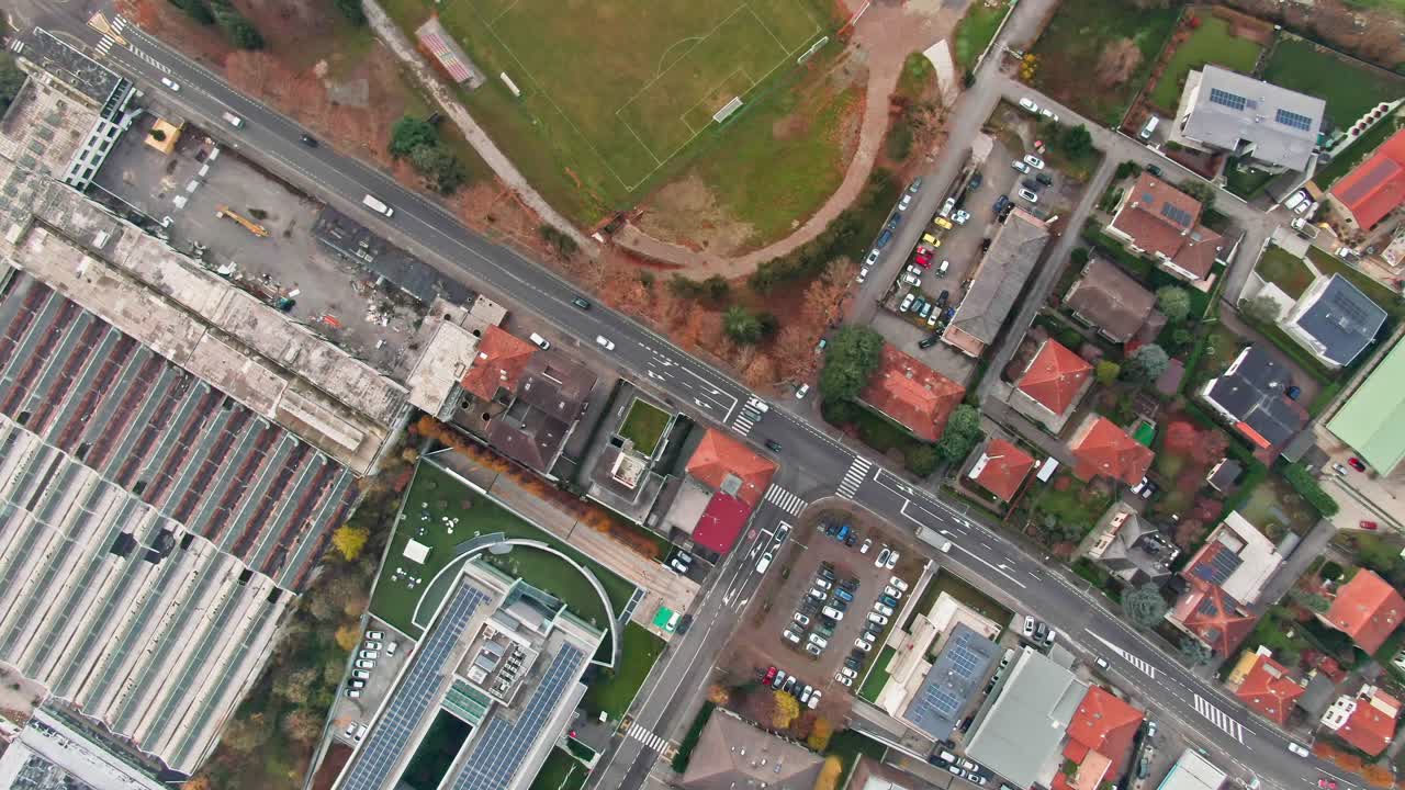 una fotografía aérea en ángulo hacia abajo por encima de una carretera, que muestra el tráfico, los edificios industriales y los campos de fútbol a continuación
