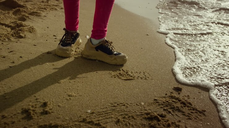 Gambe di bambina che camminano nell'acqua sulla spiaggia in riva al mare. Bambina che balla tra le onde che si infrangono.