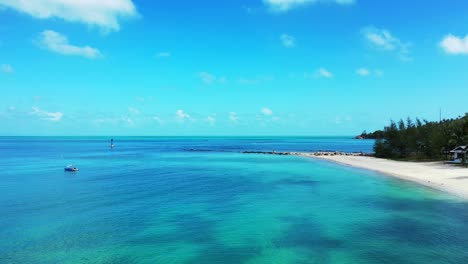 Blue-turquoise-lagoon-washing-white-sandy-beach-on-tropical-island-shore-with-green-vegetation-under-bright-sky