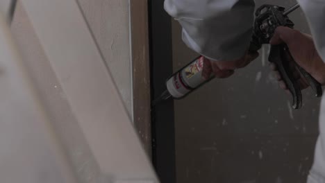 worker applying black silicone sealing with caulking gun for moisture protection on window, processing of aluminum parts in a production of aluminium windows workshop. house construction site.