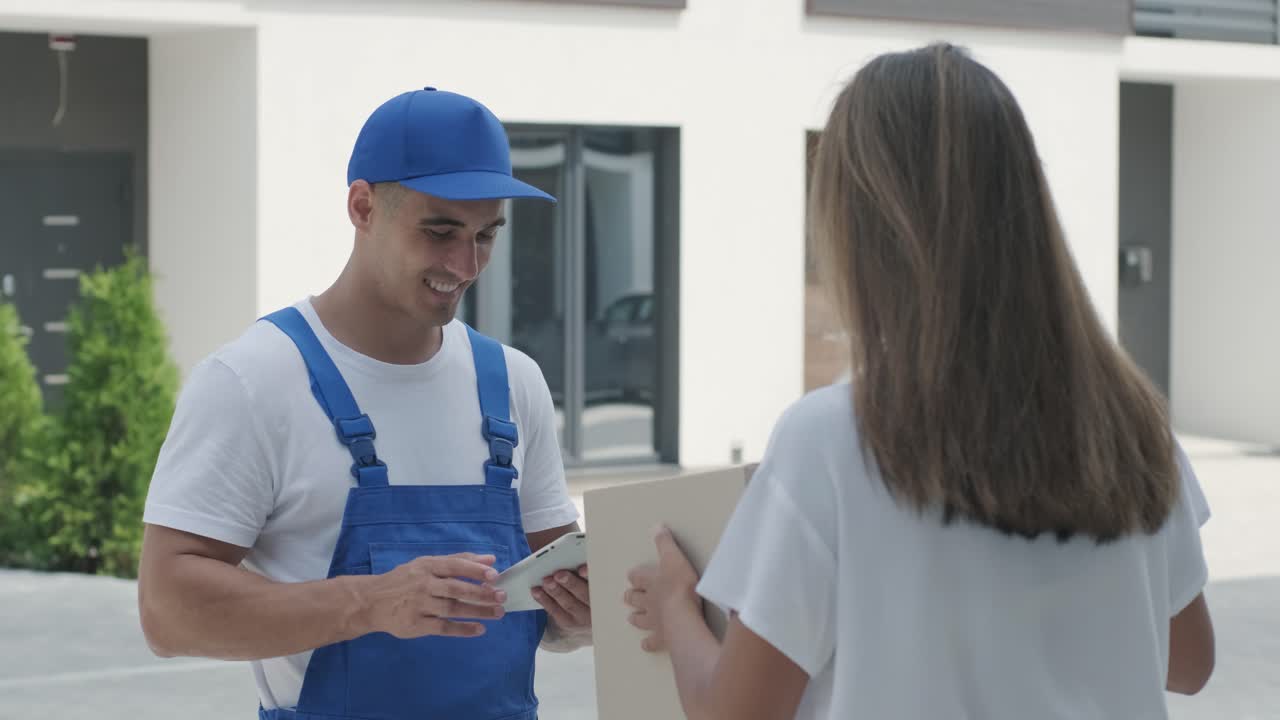 una mujer hermosa conoce a un repartidor que le da una caja de paquetes al lado de su casa, el mensajero comprueba la información en la tableta. entrega a domicilio, compras en línea