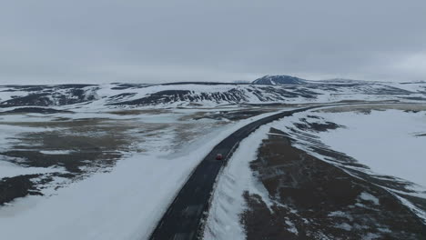 Tracking-Drohnenaufnahme-Eines-Autos,-Das-Sich-In-Der-Späten-Wintersaison-Auf-Einer-Leeren-Straße-In-Der-Wildnis-Islands-Bewegt