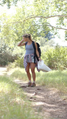 vertical video: hiking on trail, woman carrying backpack and plastic bag, enjoying nature