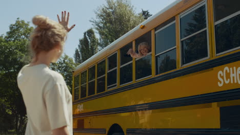 boy looking out schoolbus window waving to mom. mother sending air-kiss to son.