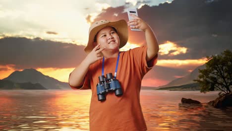 asian boy with a hat and binoculars taking a selfie on smartphone at a lake. boy researcher examines something, travel tourism adventure concept