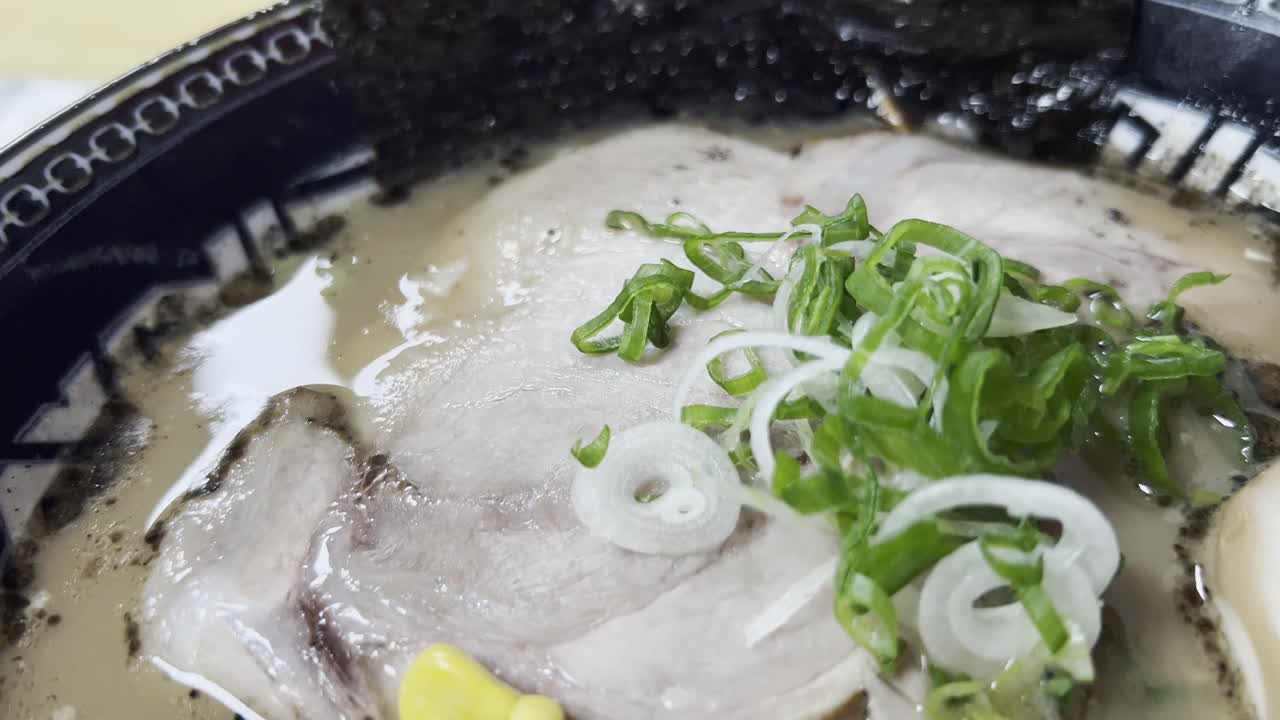 Creamy tonkotsu ramen with sliced pork, green onions and seaweed in close-up, camera zooms out