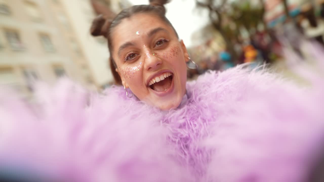 Giovane donna entusiasta con trucco glitterato e boa viola che ride a un festival