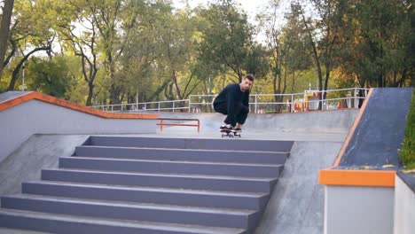 Joven-Skater-Hipster-Saltando-Escaleras-Abajo.-Truco-De-Ollie-En-Skatepark.-Tiro-En-Cámara-Lenta