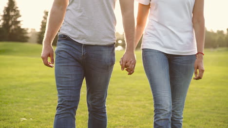 Close-Up-Of-An-Unrecognizable-Couple-Holding-Hands-And-Walking-Together-Towards-Camera-On-Meadow-In-The-Park