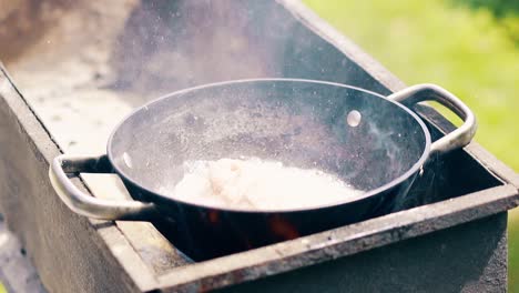 close-up slow-motion öl kocht im kessel auf kohlen auf dem grill die person fügt schweinefleisch hinzu