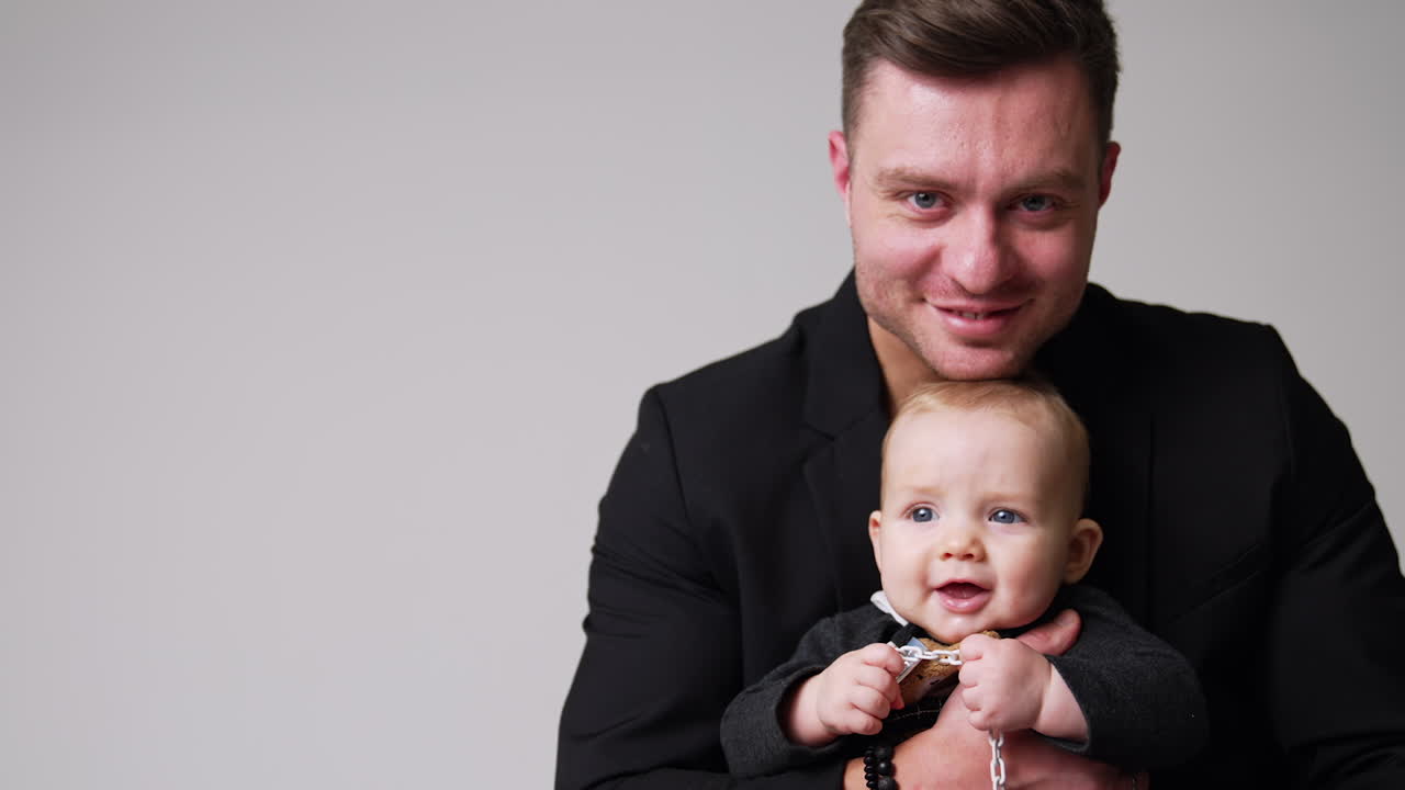 Smiling Caucasian male embracing a cute baby. Happy daddy kissing his lovely child on the head and holding him tight. White backdrop.