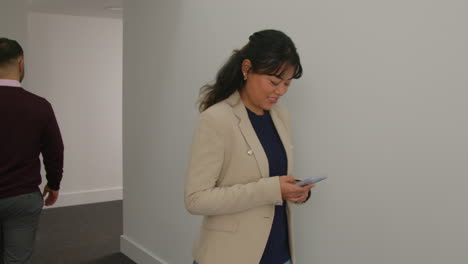 female teacher using mobile phone passing male colleague as they walk along corridor in school building